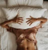 una mujer acostada en la cama con las manos sobre una almohada